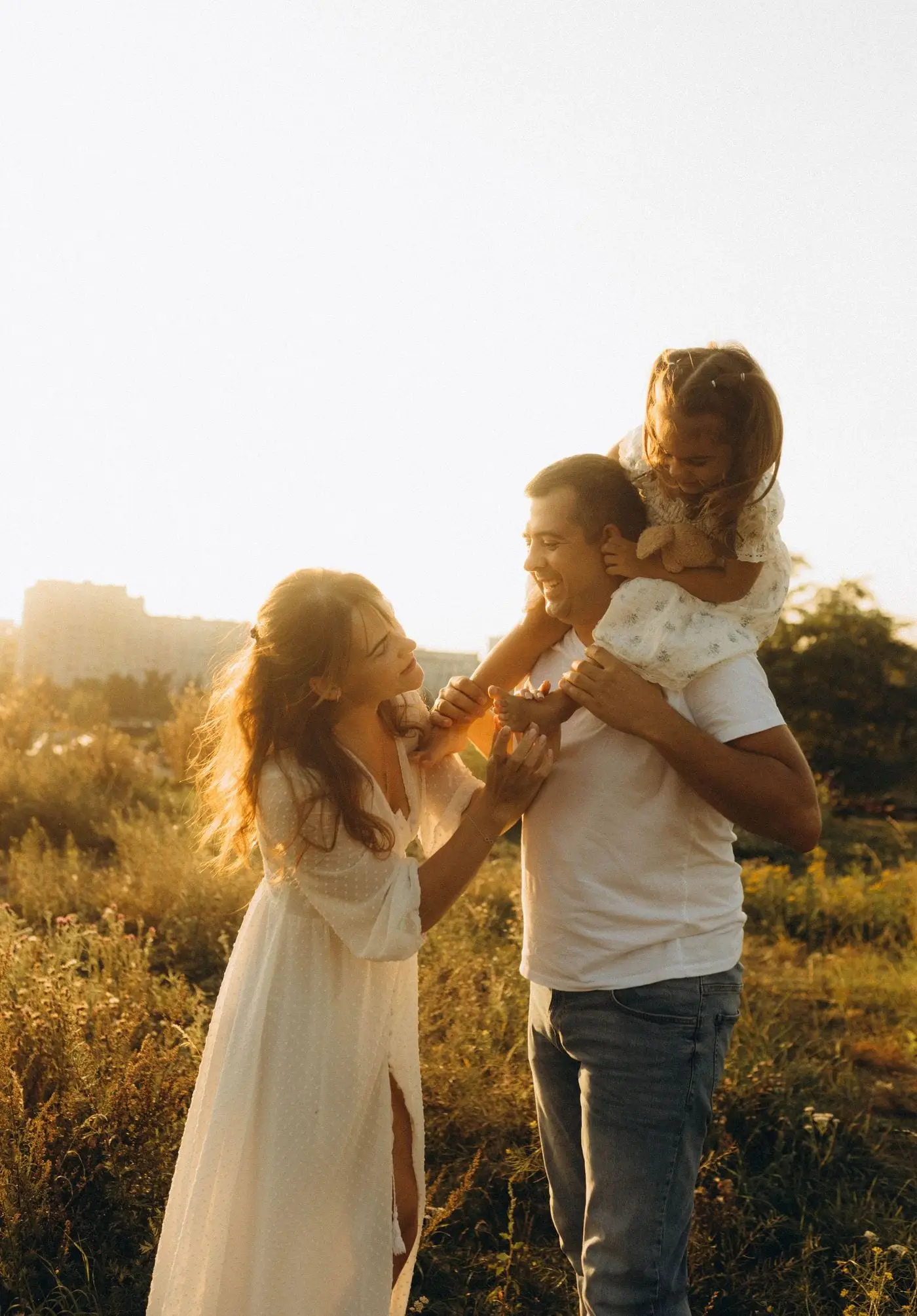 Parents and their young daughter laughing together in a field at sunset